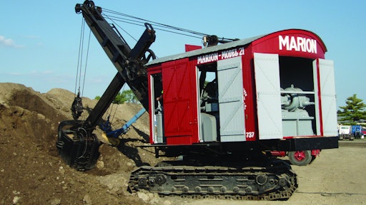 The power cord for the National Construction Equipment Museum’s Marion Model 21 Electric Shovel is visible on the ground behind it, and the AC/DC motor/generator that powers the motors can be seen inside the back doors.