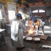 Joyworks Studio personnel inoculating a ladle of ductile iron.