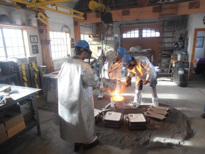 Joyworks Studio personnel inoculating a ladle of ductile iron.