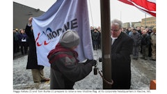 Modine President and CEO Tom Burke (right) prepare to raise the flag with the company's 100th anniversary graphic and logo at its headquarters.