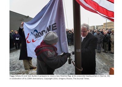 Modine President and CEO Tom Burke (right) prepare to raise the flag with the company's 100th anniversary graphic and logo at its headquarters.