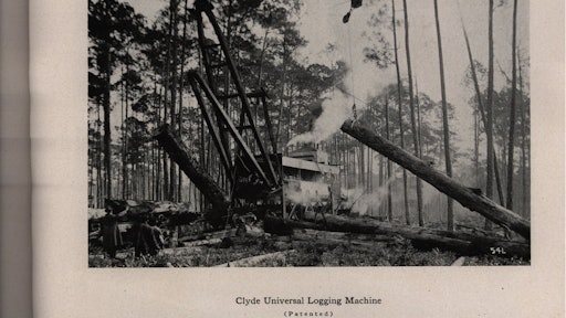 A Clyde Universal Logging Machine hauls one log in by cableway while positioning another for loading onto a rail car passing beneath it. An incline carries the car over the track upon which the logging machine sits.