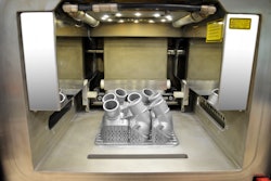 The view into the interior of the 3D printer shows the first printed thermostat covers, which are still connected to the work platform. After removal of the platform and support structure, the aluminum/silicon metallic powder is removed by suction, sieved, cleaned and ecologically fed back into the recycling system.