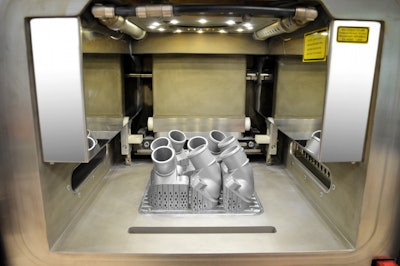 The view into the interior of the 3D printer shows the first printed thermostat covers, which are still connected to the work platform. After removal of the platform and support structure, the aluminum/silicon metallic powder is removed by suction, sieved, cleaned and ecologically fed back into the recycling system.
