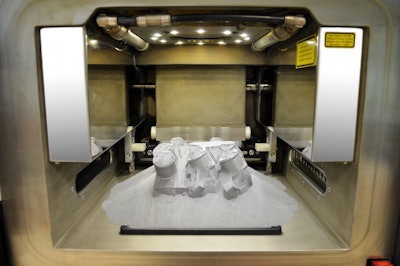 The photo shows the working cavity of the laser printer at whose center a metallic thermostat cover has been produced for the first time using selective laser melting (SLM). When the work platform is raised, the powdered aluminum/silicon material moves to the side and the contours of the component become visible.