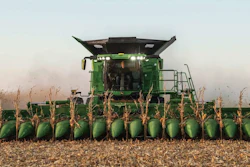 Green John Deere combine harvester with corn header harvesting corn field at dusk