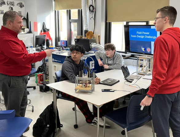 Students and instructor collaborate around a table with engineering equipment during a Field Power Team Design Challenge workshop.