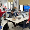 Students and instructor collaborate around a table with engineering equipment during a Field Power Team Design Challenge workshop.
