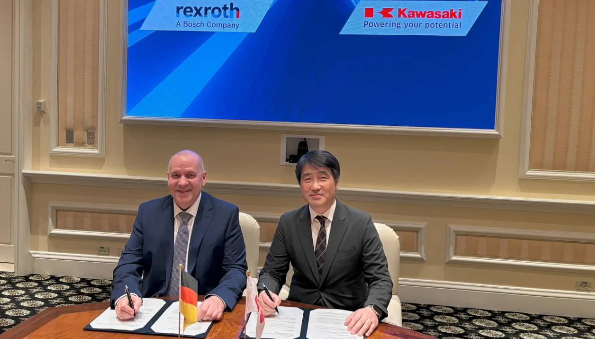 Two businessmen sign documents at formal meeting with Rexroth and Kawasaki logos displayed on screen behind them