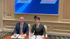 Two businessmen sign documents at formal meeting with Rexroth and Kawasaki logos displayed on screen behind them