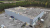 Aerial view of large white warehouse building under construction surrounded by forest with materials on roof