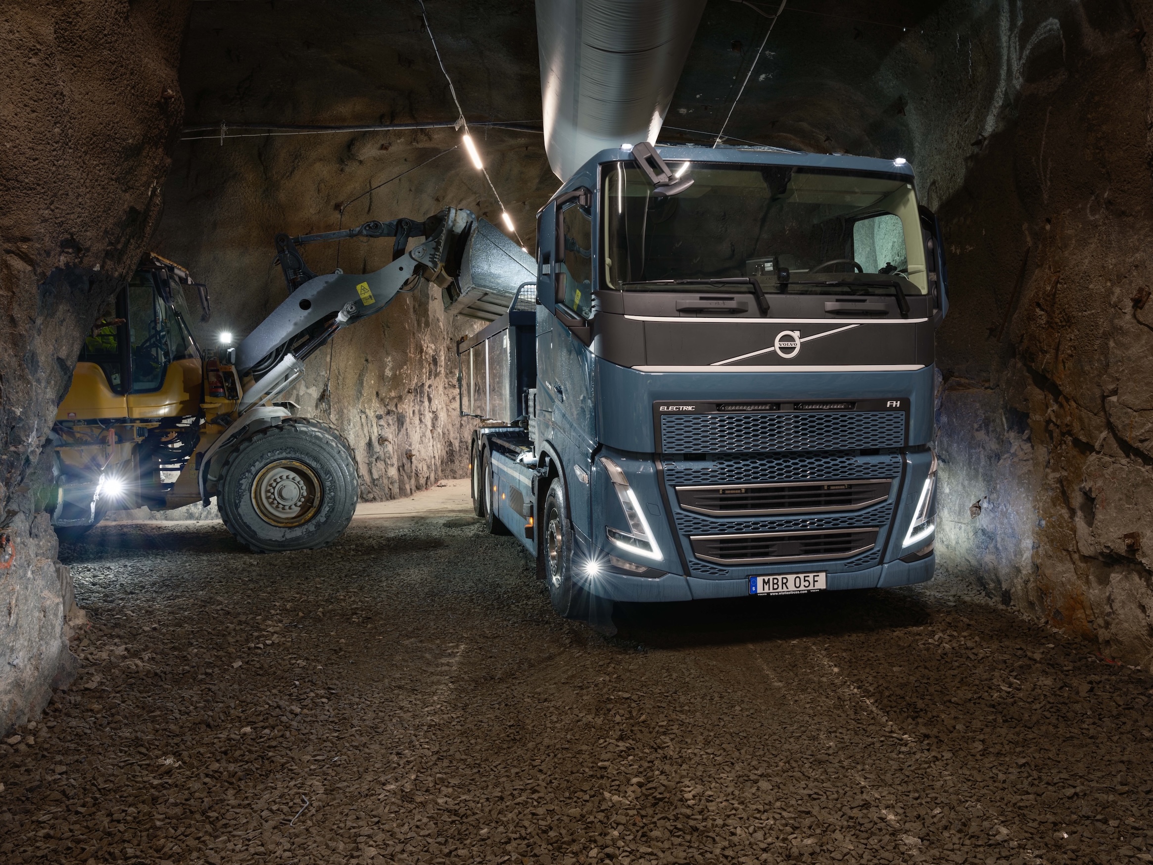 Volvo truck and wheel loader loading material in an underground mining tunnel at night