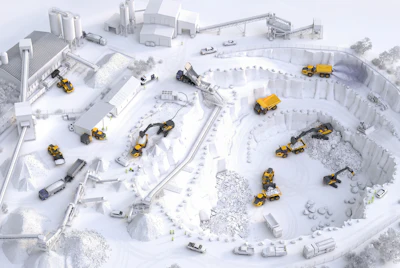 Aerial view of active construction site with yellow heavy machinery, equipment, and materials scattered across snowy ground with industrial buildings